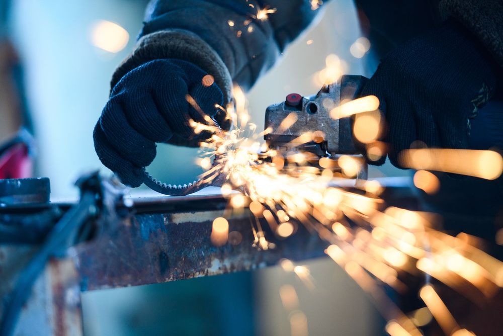 Gloved hands grinding metal, sending bright sparks in a workshop