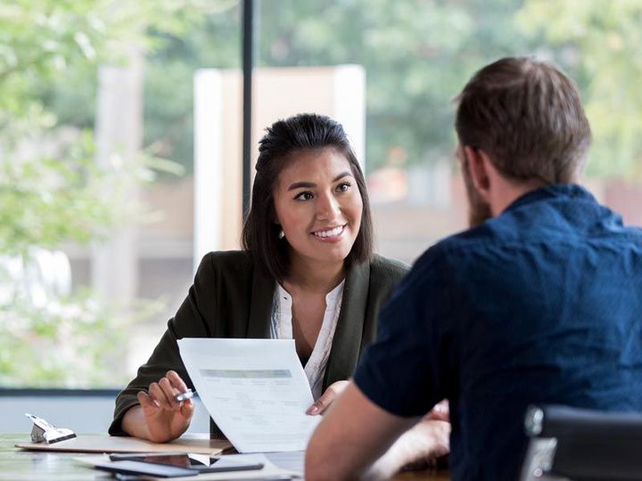 Two people meeting at a table, smiling and discussing a document in a bright office.