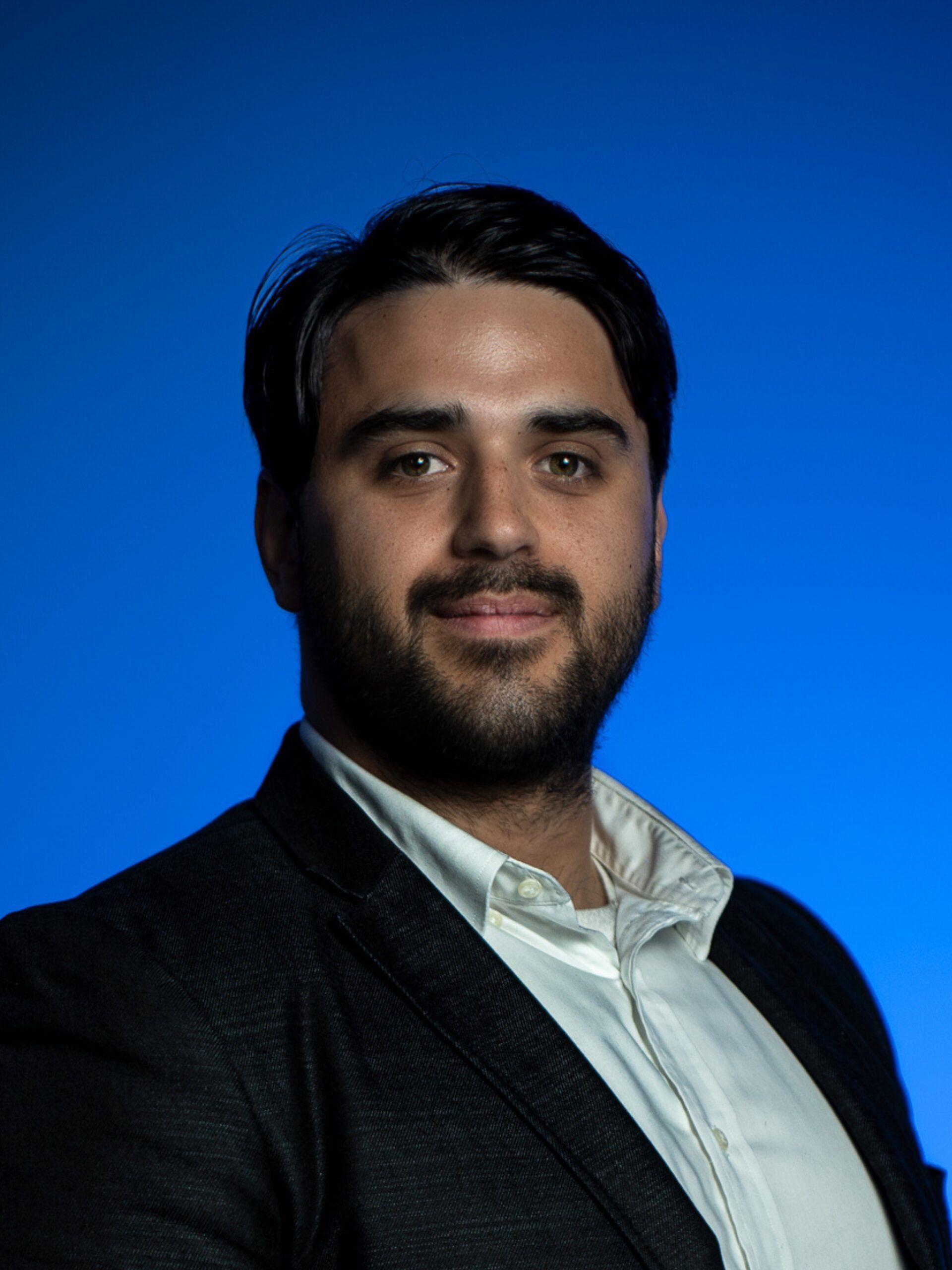 Portrait of a smiling man in a dark blazer and white shirt against a blue background