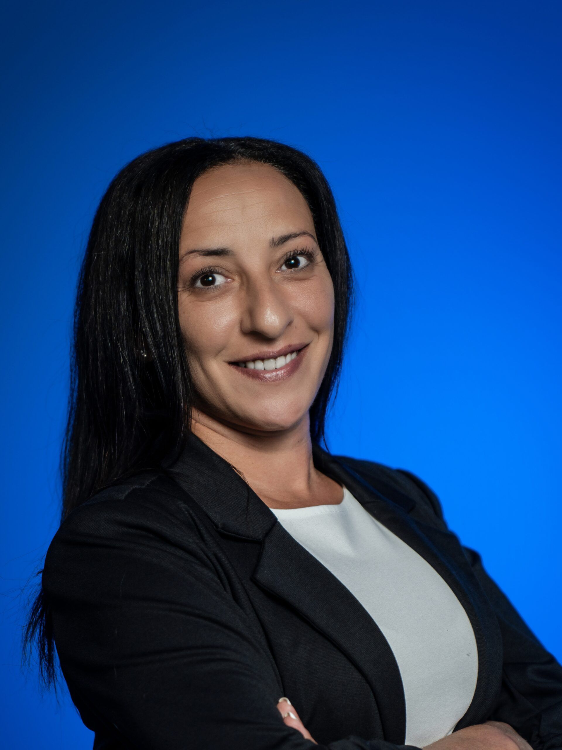 Portrait of a smiling person in a black blazer against a blue background