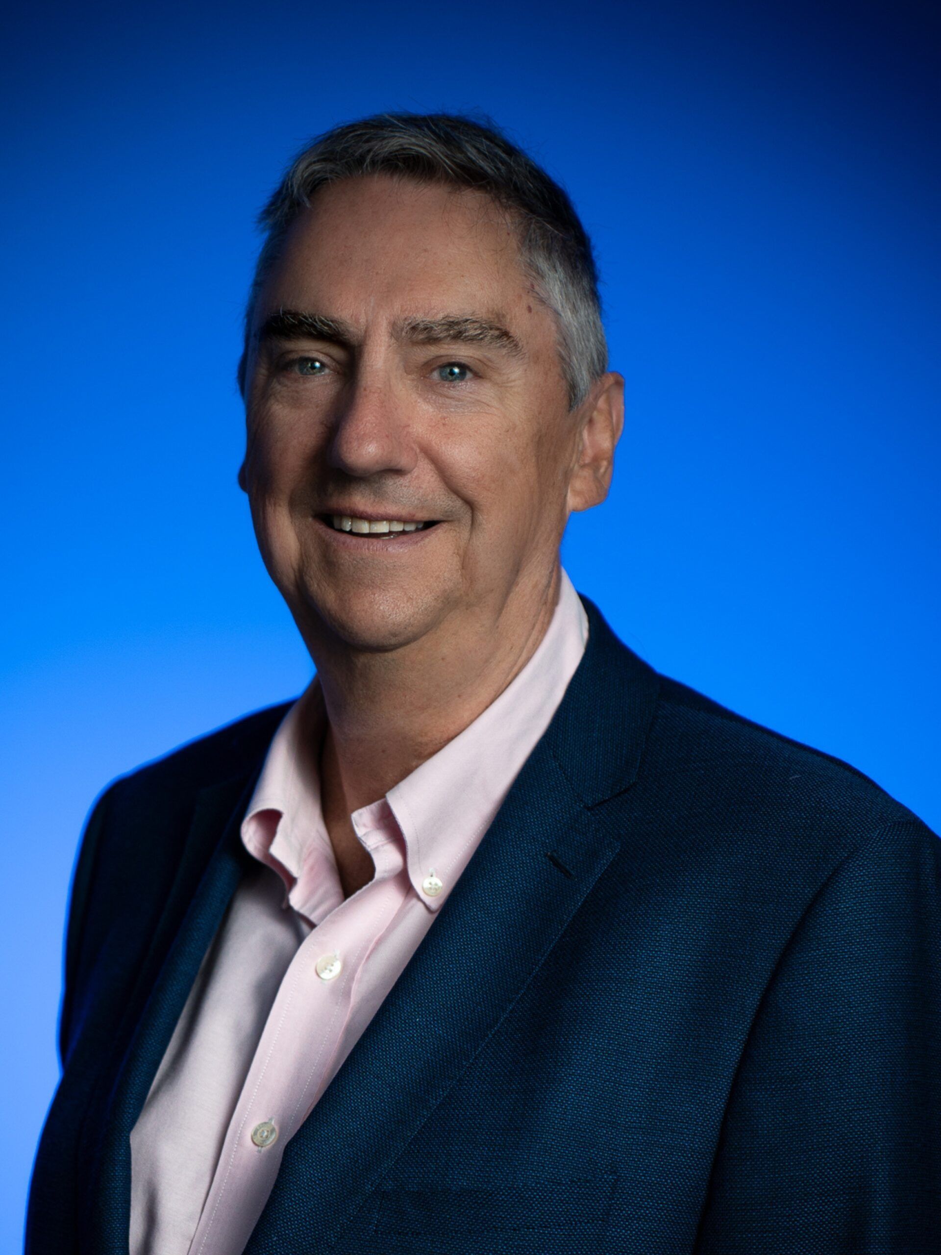 Smiling man in a dark blazer and light shirt against a blue gradient background