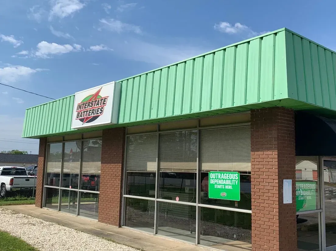 Exterior view of a commercial building with green awning, glass windows, and a brick facade; a sign with a logo is visible.