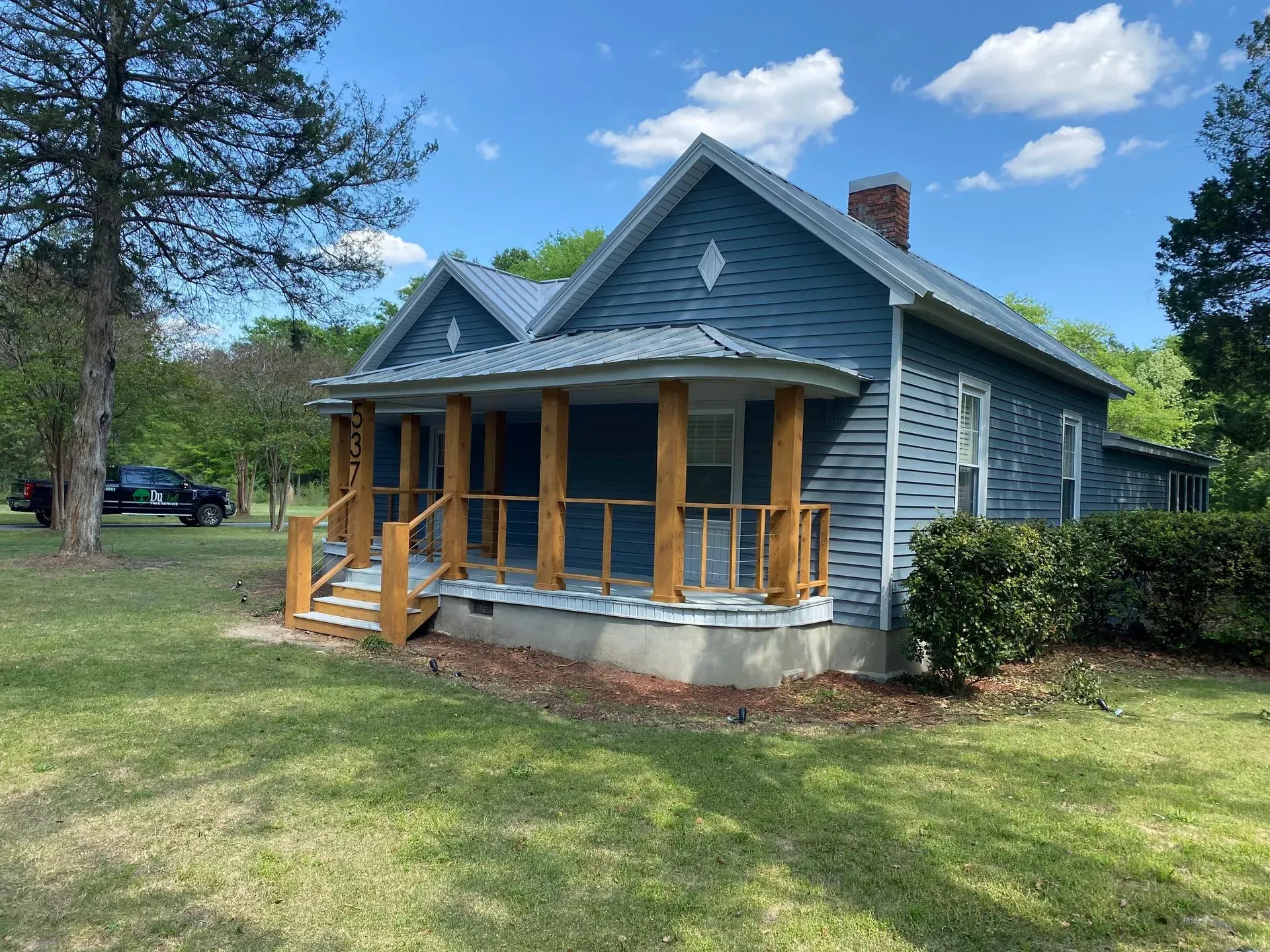 Blue house with wooden porch and pillars, set on a grassy lawn with a blue sky.