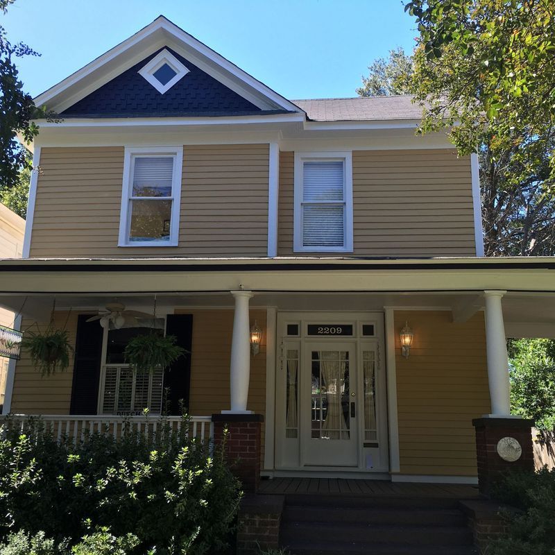 Yellow two-story house with white trim, porch, and a blue gable.