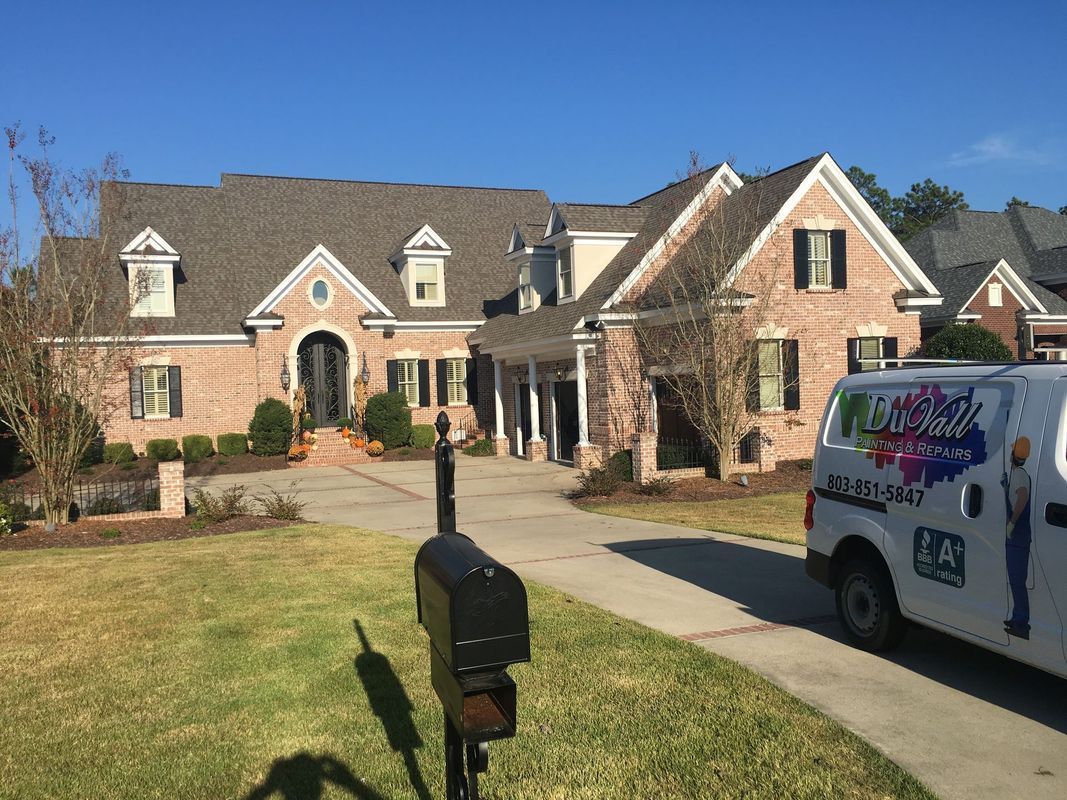 Brick house with a long driveway and a white van in front.