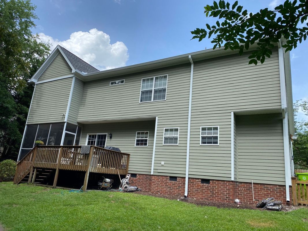 Two-story house with green siding, a wooden deck, and a screened porch under a blue sky.