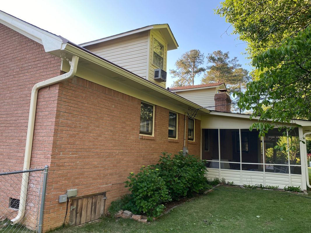 Brick house exterior with a screened porch, chimney, and yard with green grass and bushes.