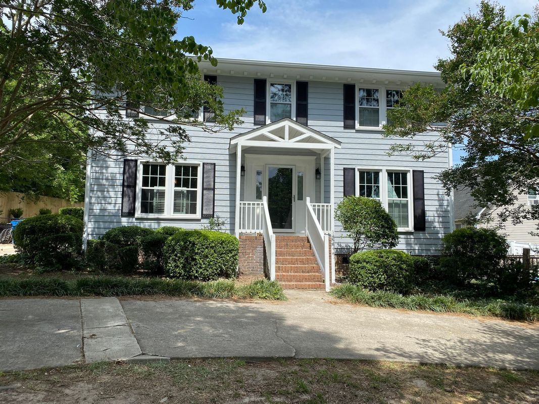 Two-story house with light blue siding, black shutters, white trim, and a brick entrance.