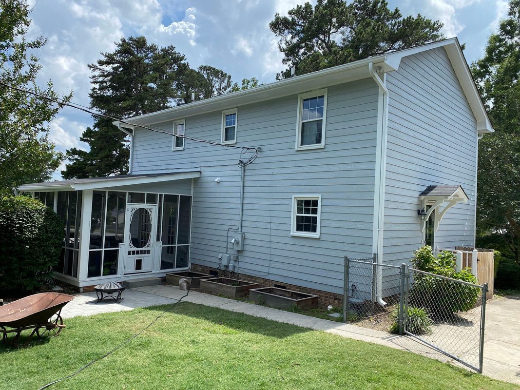 Light blue two-story house with a screened porch, windows, and a green lawn. Trees and a wheelbarrow are in the yard.
