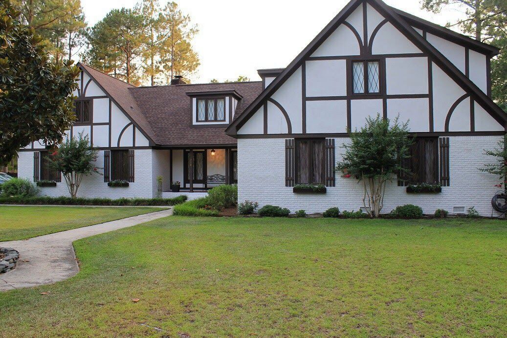Tudor-style house with white stucco walls, dark wood accents, and a brown roof.