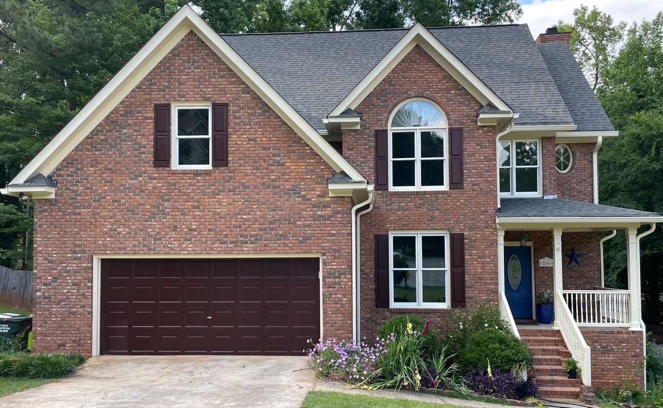 Brick two-story house with brown garage door, shutters, and blue front door.