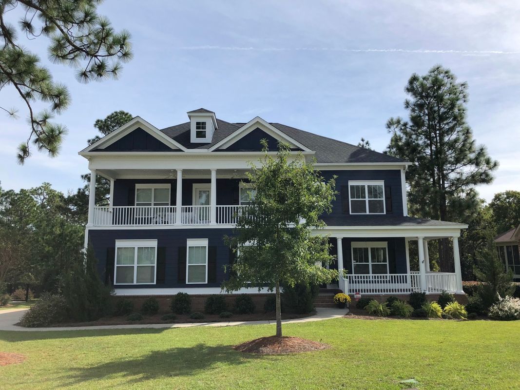 Two-story blue house with white trim and wraparound porch, on a green lawn.