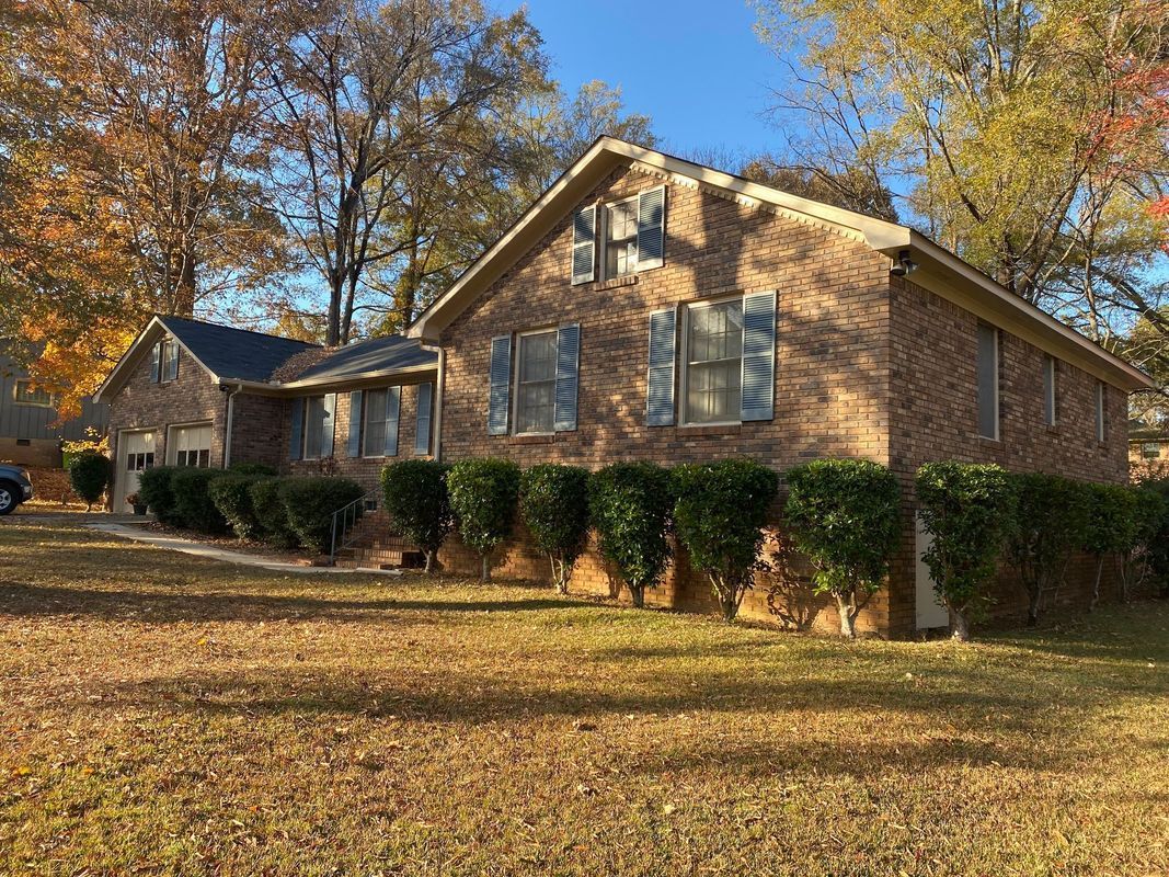 Brick house with shutters, surrounded by trimmed bushes and trees with fall foliage.
