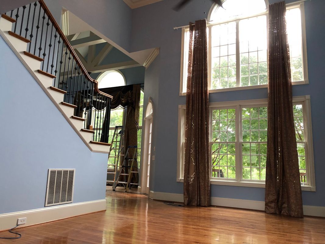 Light blue interior with a staircase and large windows, brown curtains, hardwood floors.