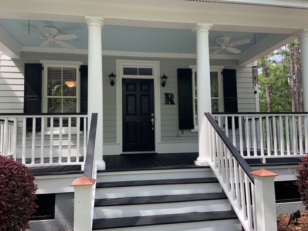 Front porch of a light gray house with black accents and white columns, steps, and railing.