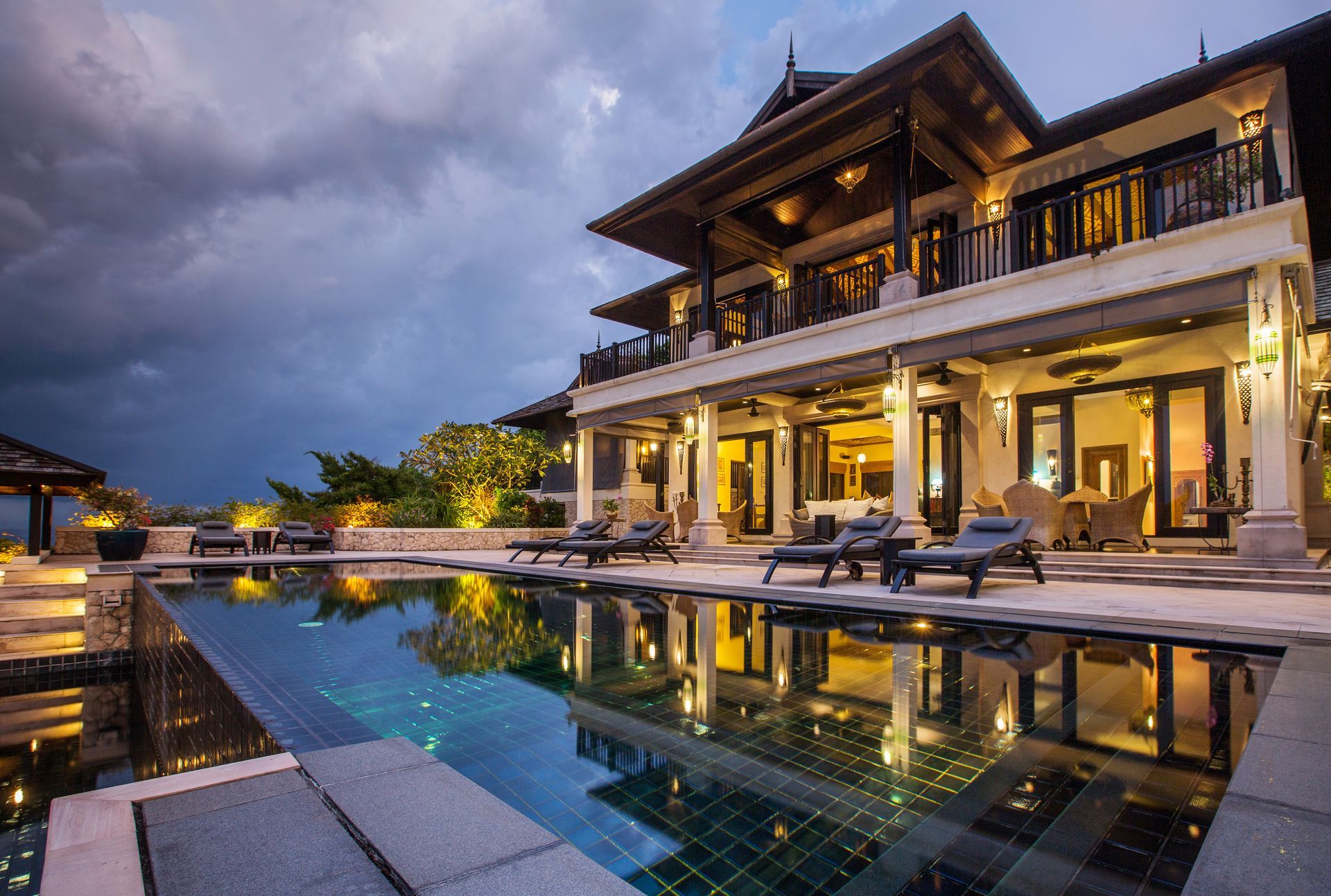 Luxury villa at dusk with a lit infinity pool reflecting the building and cloudy sky