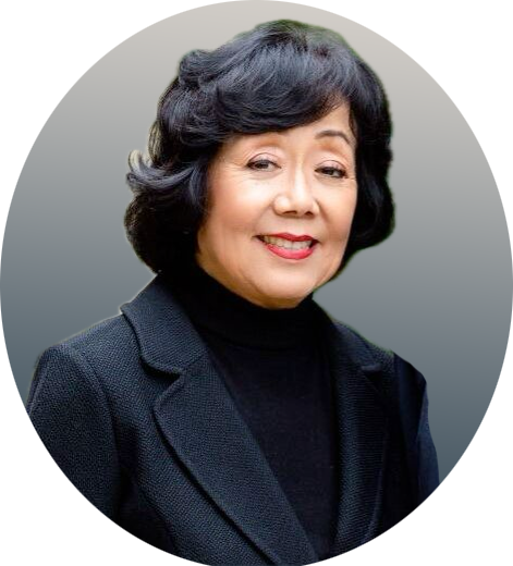 Portrait of a woman in a dark blazer and black turtleneck, smiling against a gray background