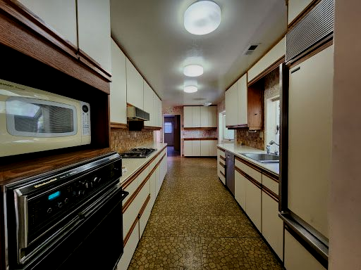 Long galley kitchen with wood cabinets, stainless appliances, and bright ceiling lights