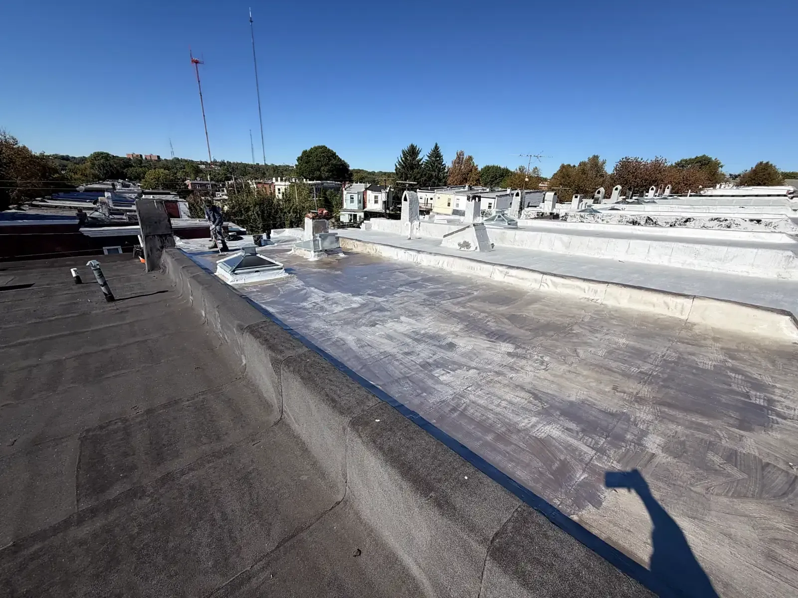 Two neighboring rowhouse flat roofs, the left one dark and uncoated, the right one freshly silver coated