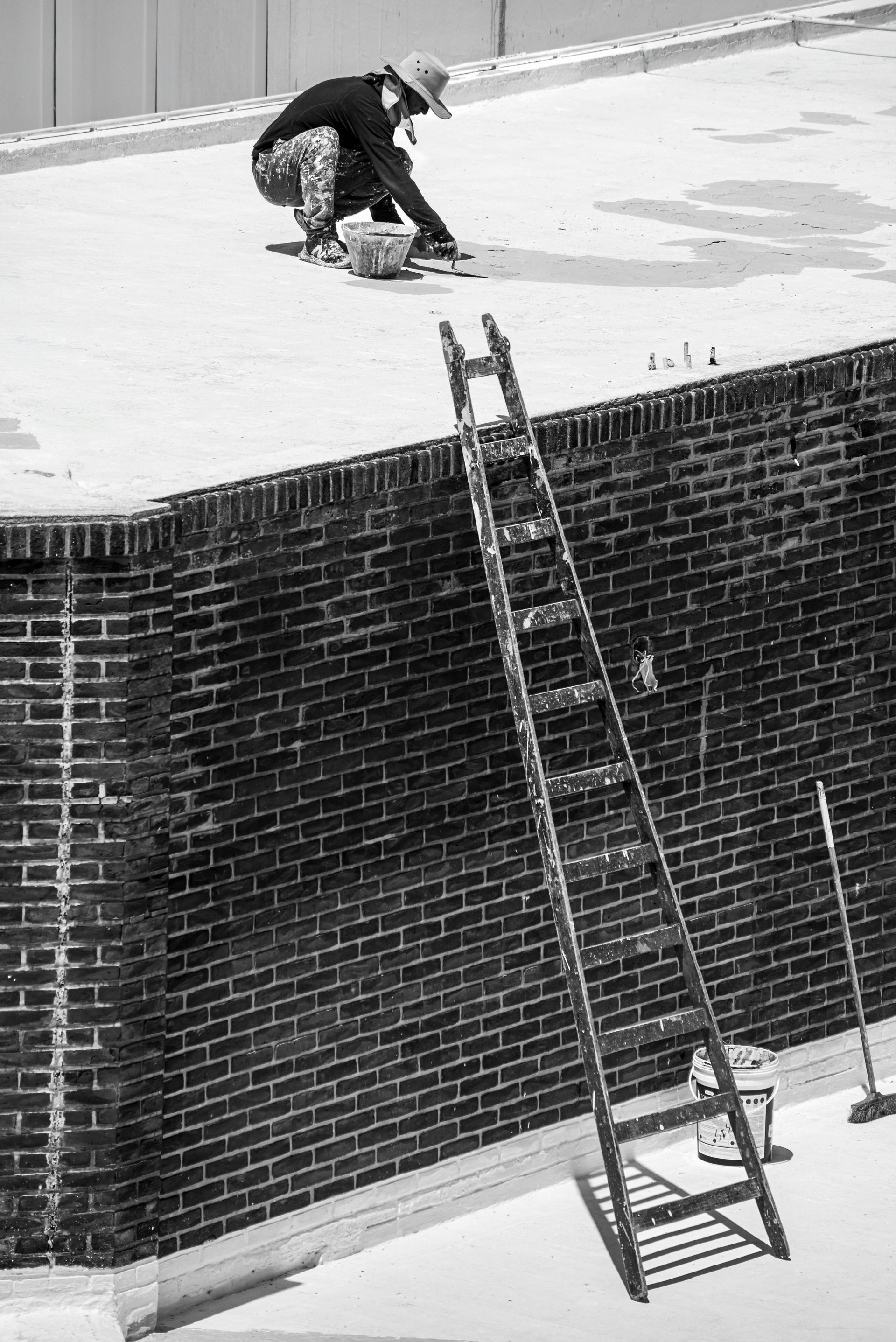 A black and white photo of a man painting a brick wall