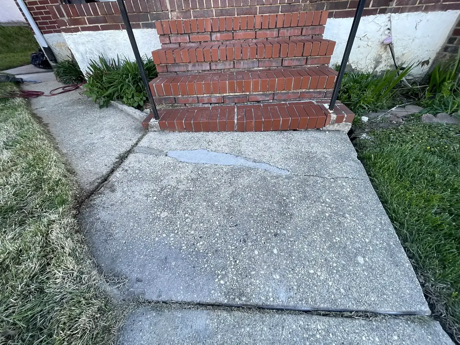 Cracked, sunken concrete sidewalk slab at the bottom of brick front steps