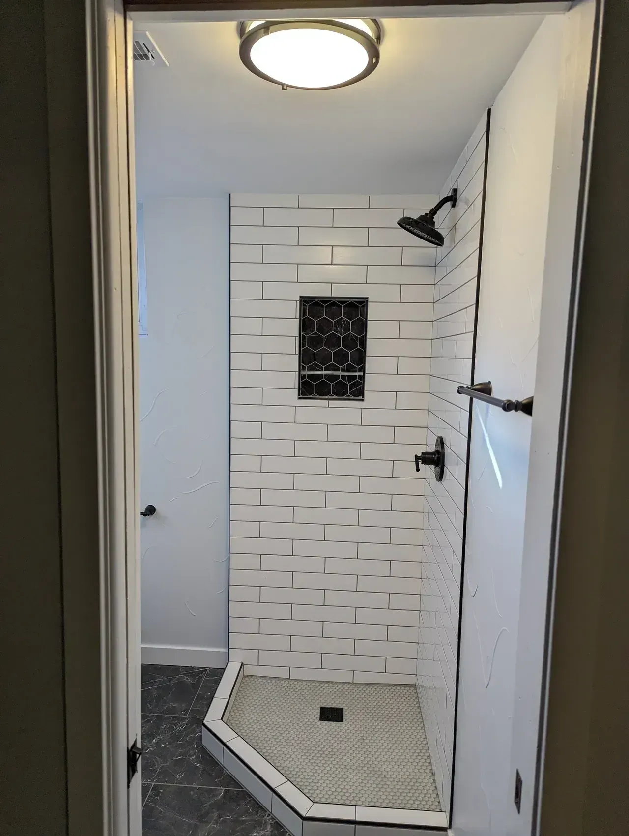 Bathroom with white subway tile shower, black fixtures, and mosaic floor.