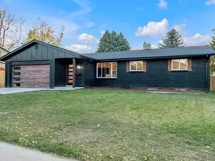 Black house with wooden garage door and accents, green lawn, blue sky.