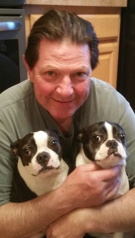 A man is holding two boston terrier puppies in his arms.