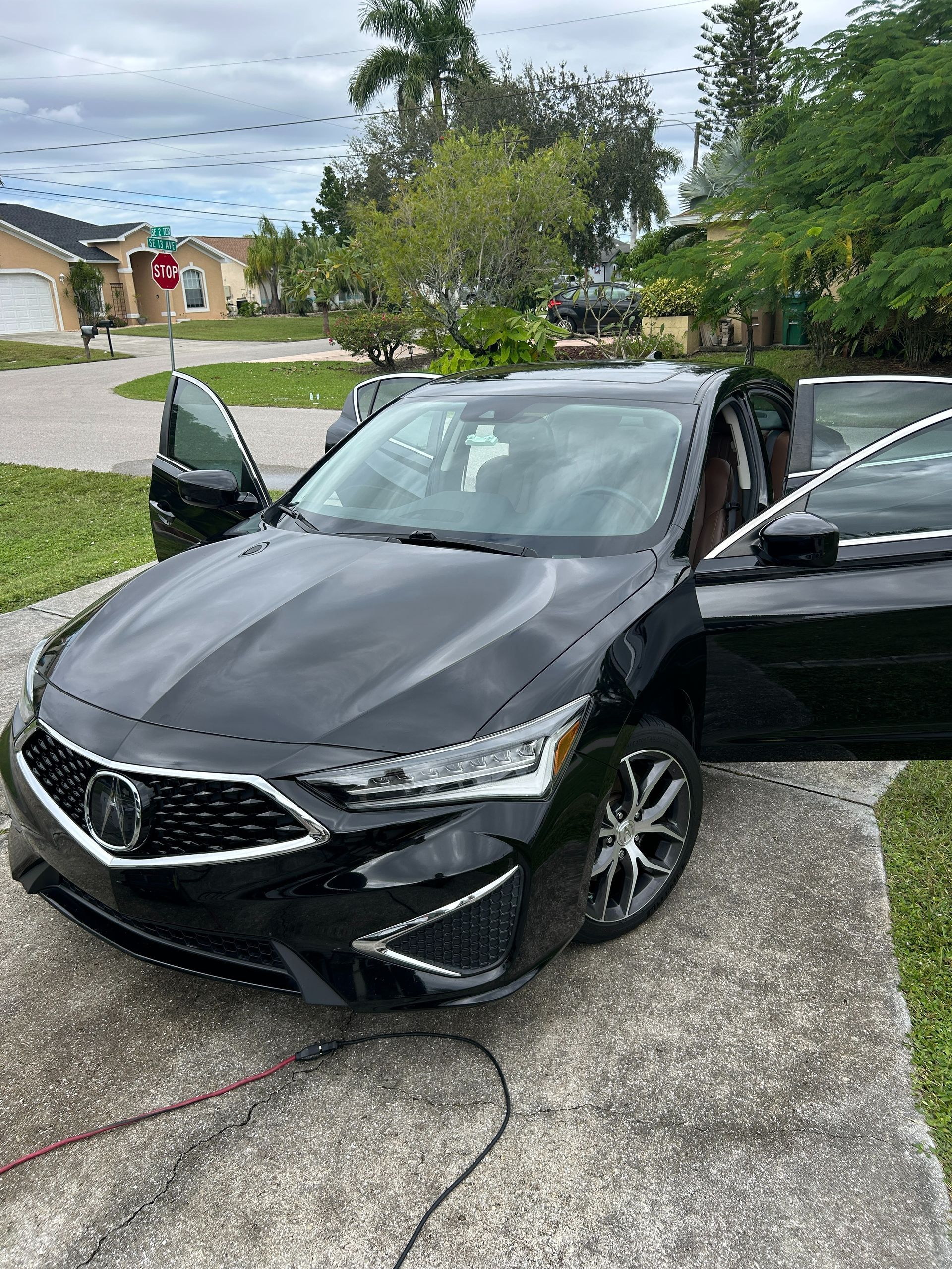 Black sedan with both front doors open, parked on a driveway in a suburban yard.