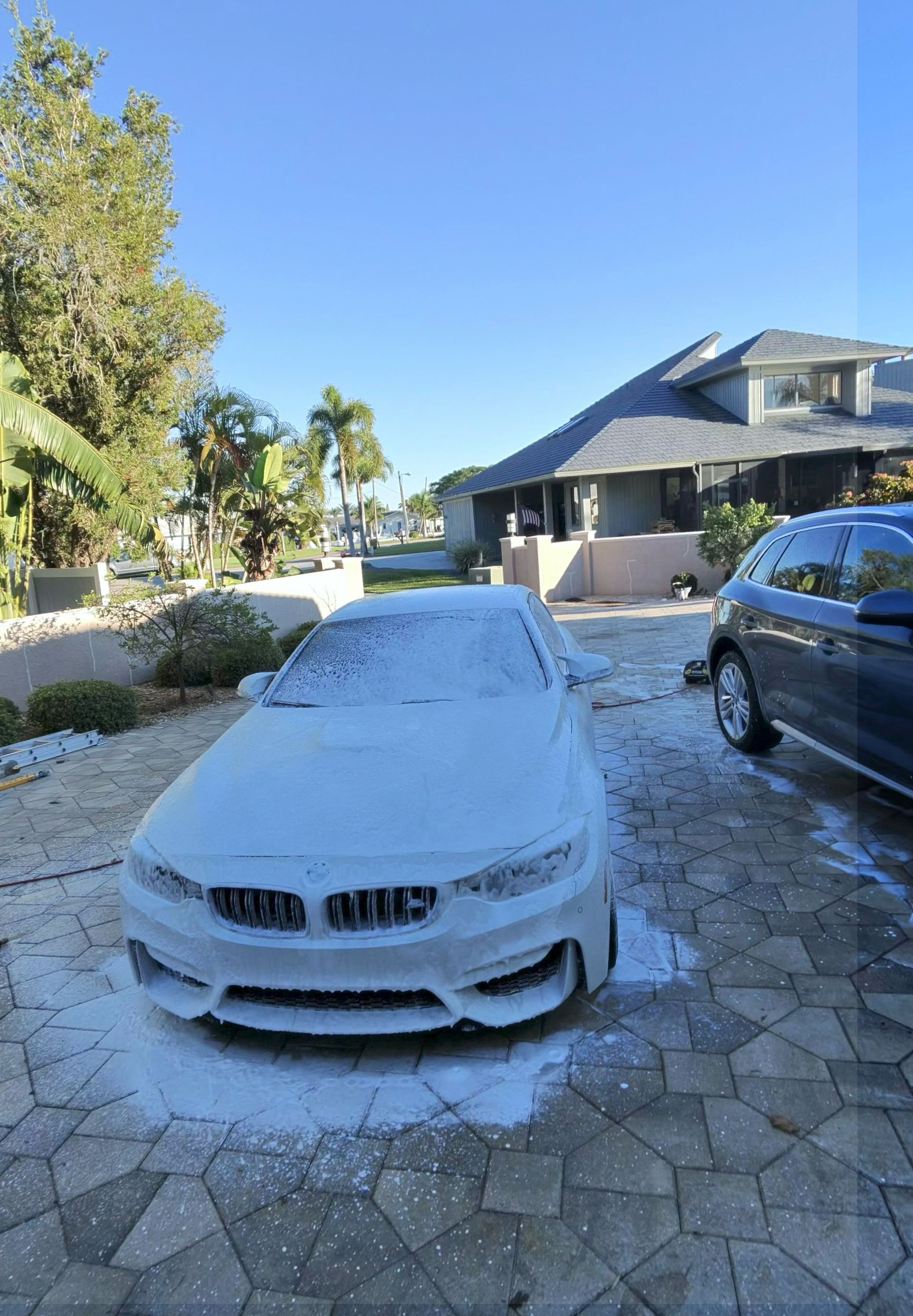 White BMW parked in a sunny driveway beside a house and trees