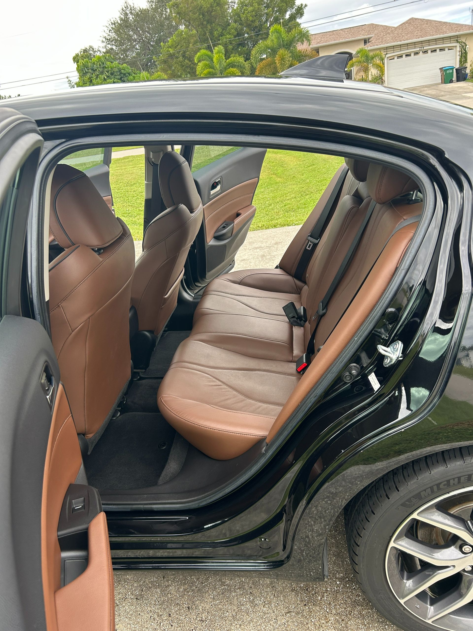 Open car door showing tan leather back seat and black exterior, parked outdoors.