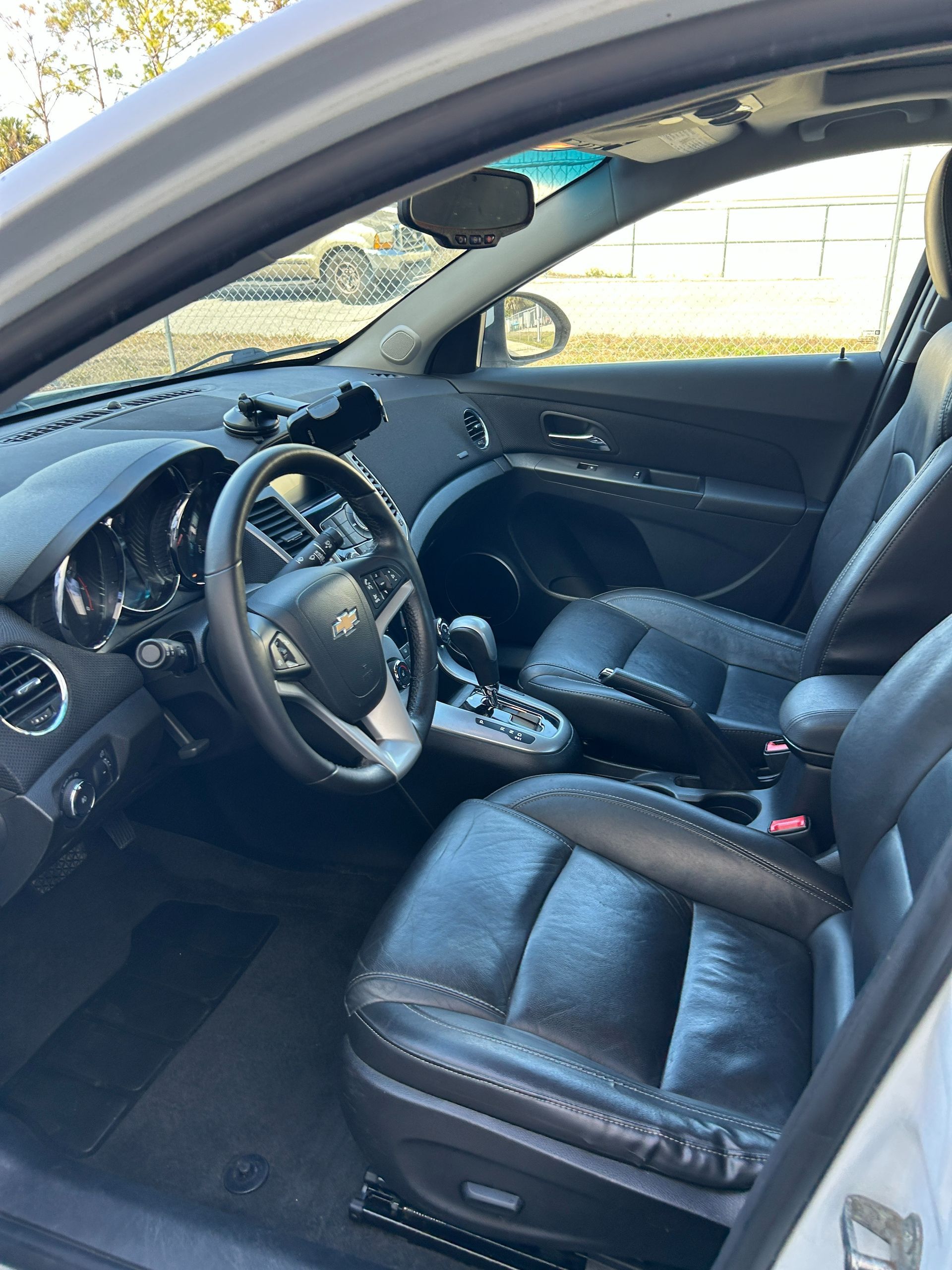 Car interior with black leather seats, steering wheel, and dashboard, viewed from the open driver’s door