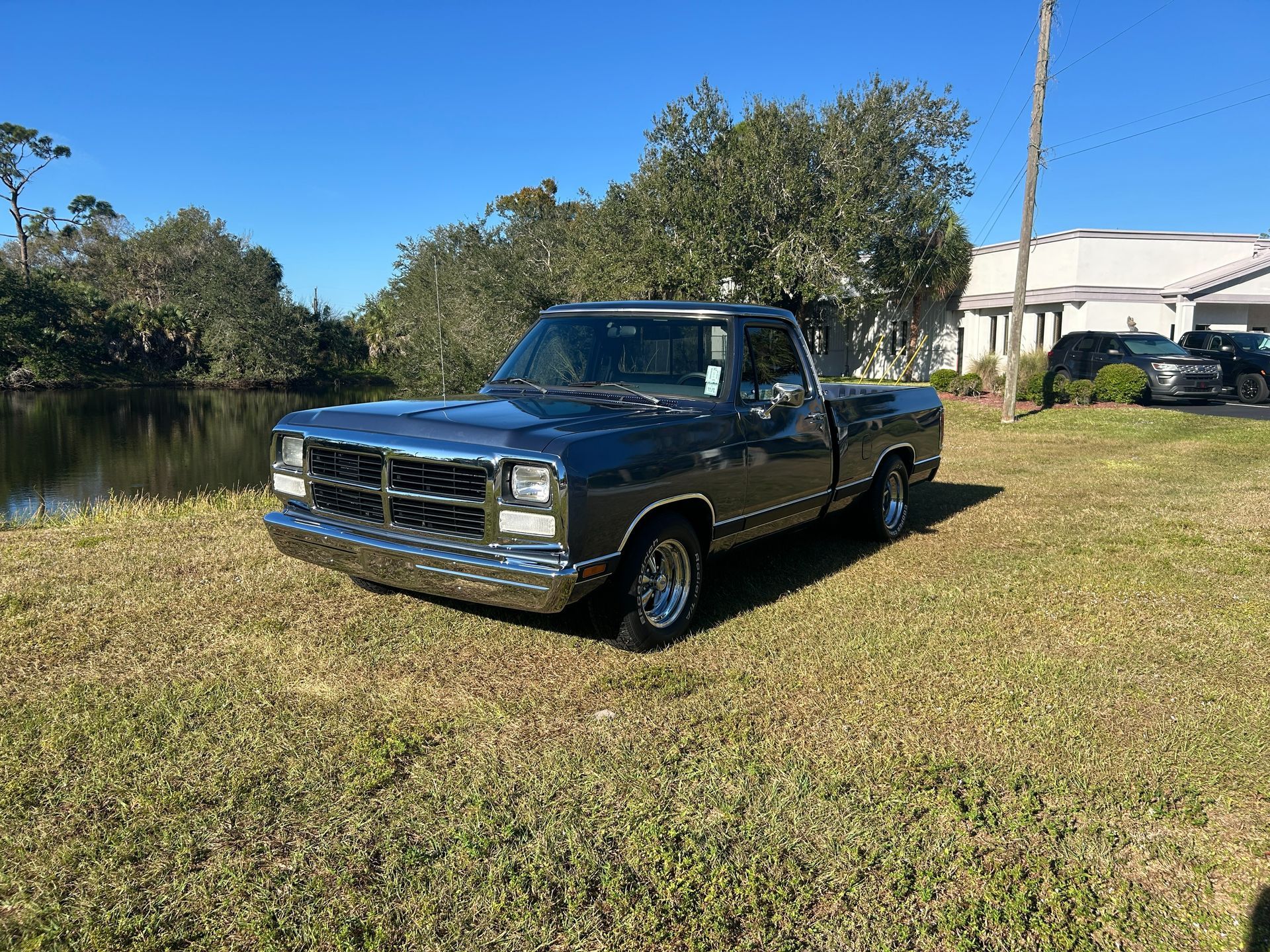 Blue pickup truck parked on grass beside a calm river under a clear sky