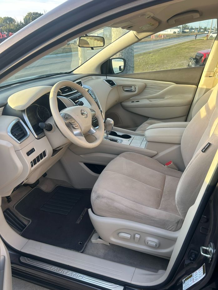 Open car door showing beige interior, driver's seat, steering wheel, and center console.
