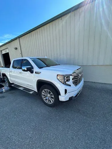 White GMC pickup truck parked beside a beige industrial building on a paved lot.