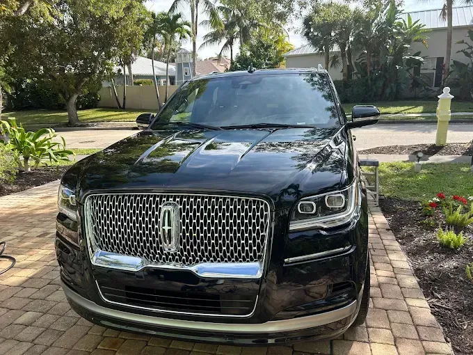Black Lincoln SUV parked on a brick driveway in a sunny residential yard with palm trees