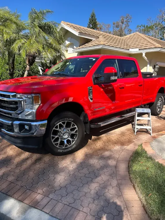 Bright red pickup truck parked in a sunny driveway beside a house, with a small step stool nearby