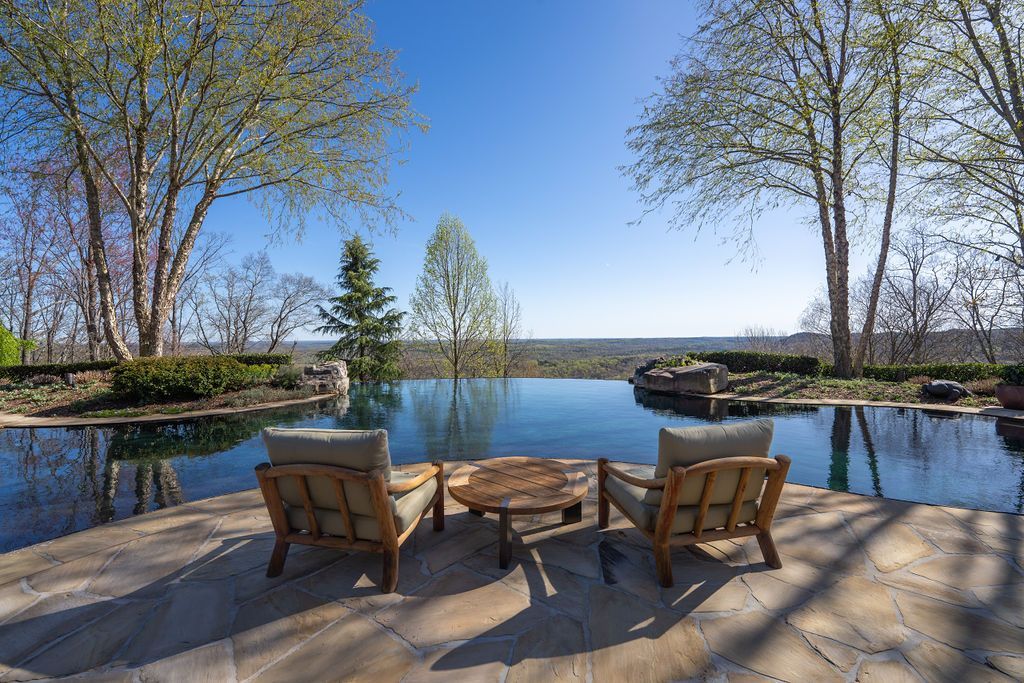 There are two chairs and a table in front of a large swimming pool.