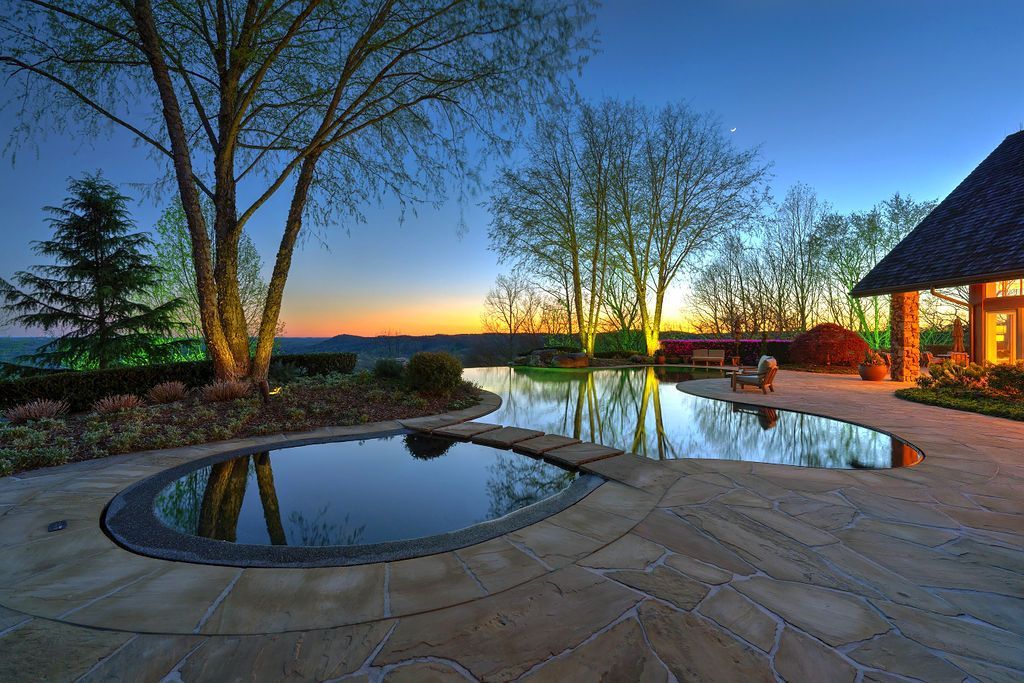 Tranquil dusk scene with a reflective pool and building, trees, and sunset sky.
