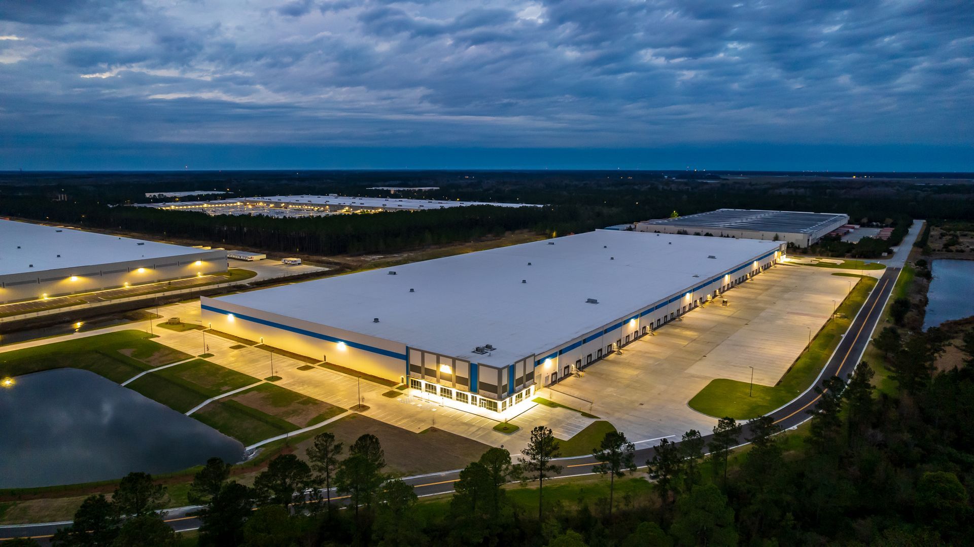 An aerial view of a large warehouse at night surrounded by trees and water.