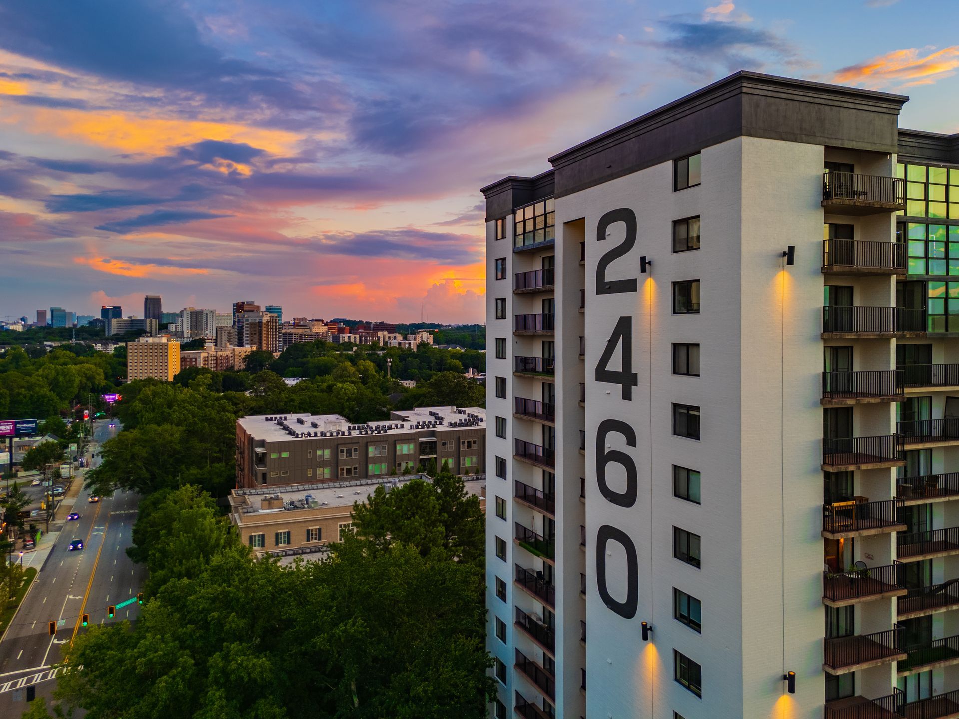 High-rise apartment building with the number 2460 in large black digits. A cityscape and colorful sunset in the background.