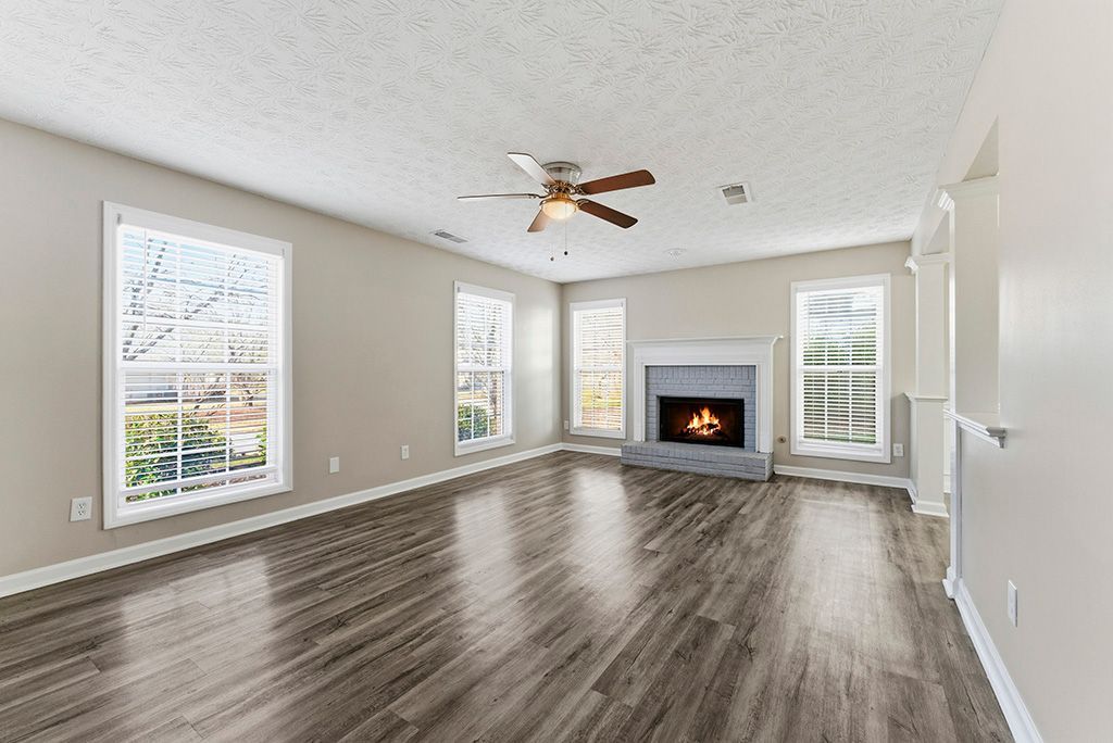 Empty living room with fireplace, windows, and wood flooring.
