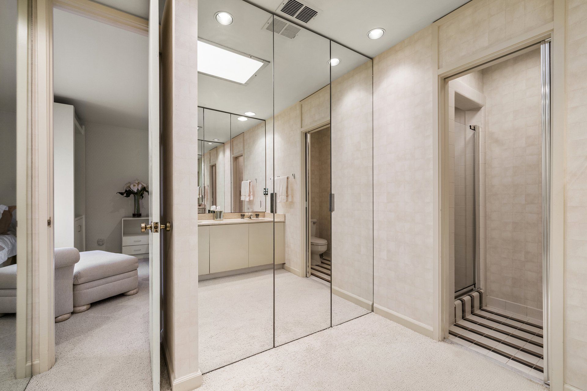 A walk in closet with mirrored doors leading to a bathroom and bedroom