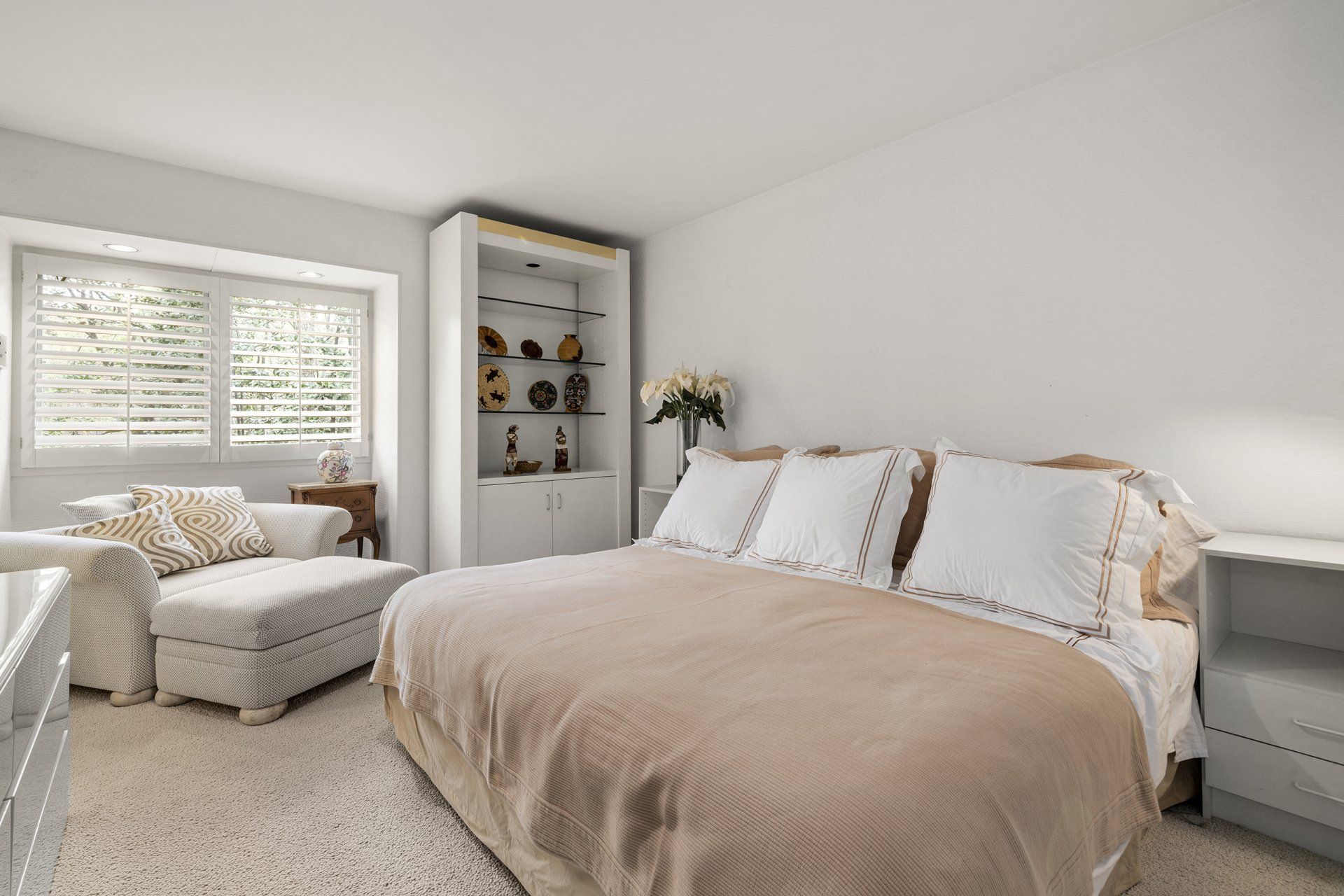 A bedroom with a bed , chair , nightstand , shelves and a window.