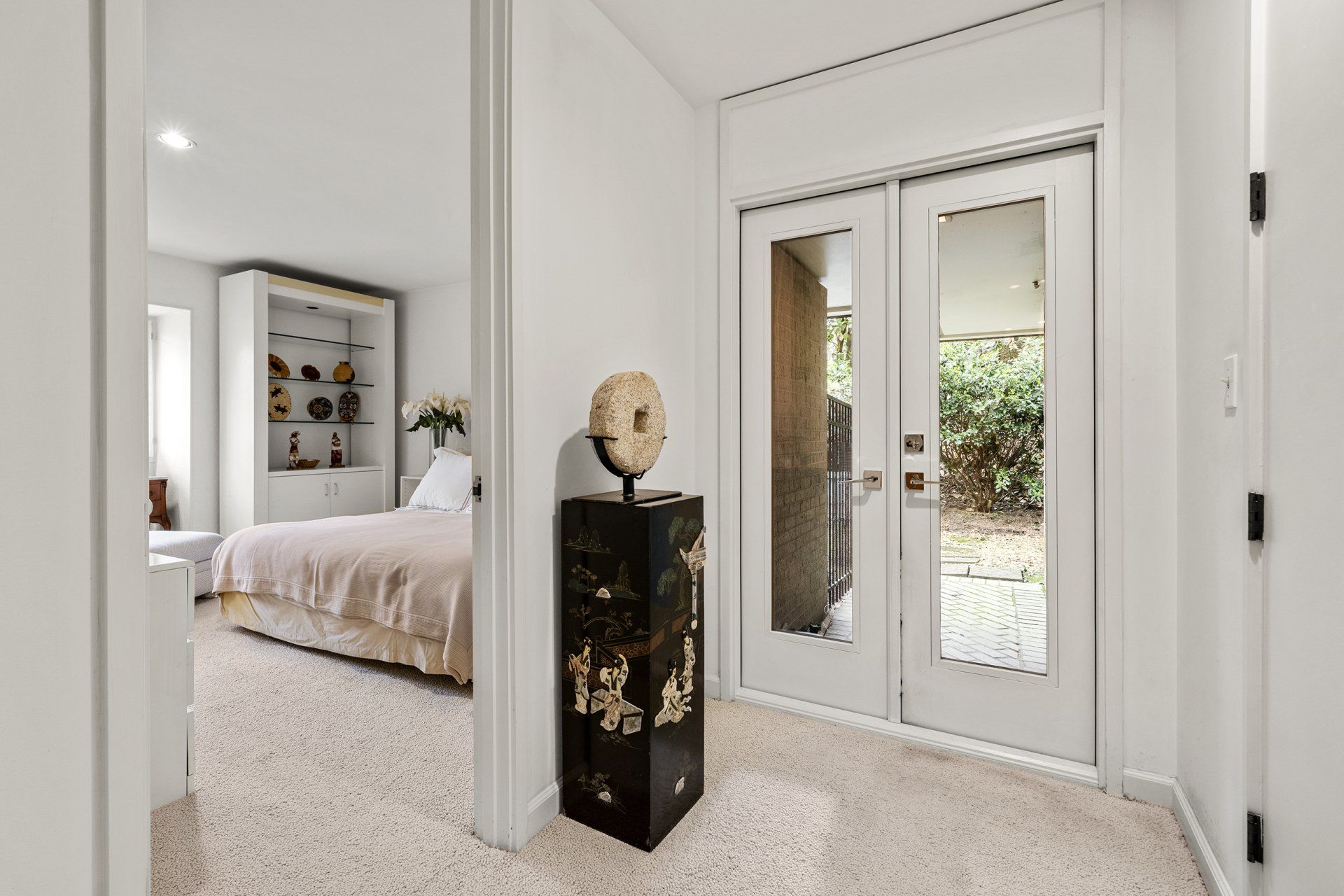A hallway leading to a bedroom with a bed and a mirrored door.