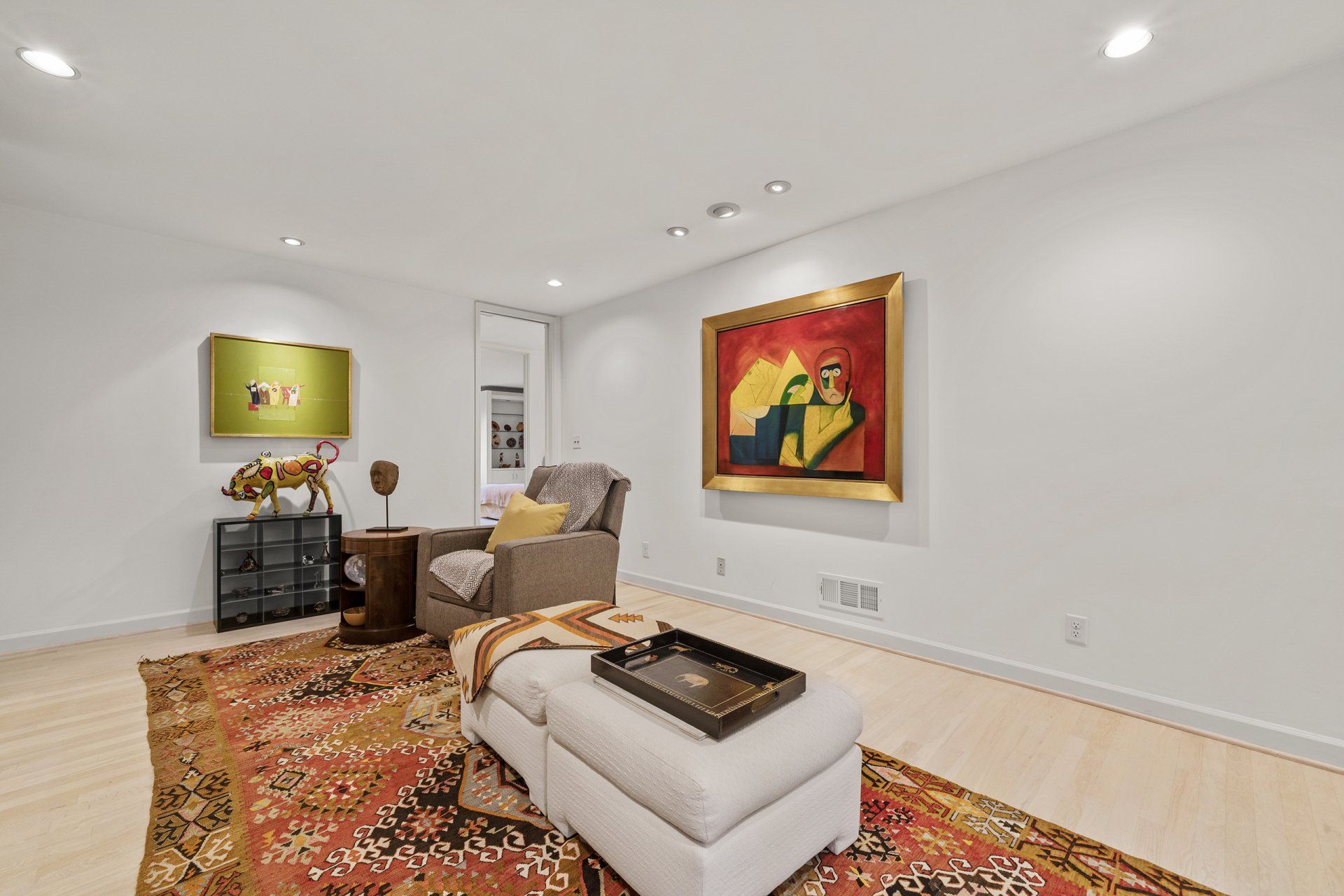 A living room with a rug , ottoman , chair and painting on the wall.