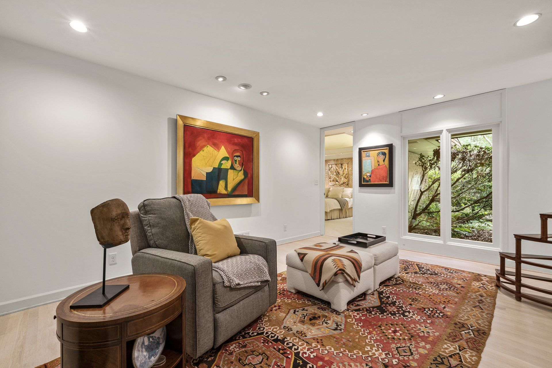 A living room with a chair , ottoman , table and paintings on the wall.