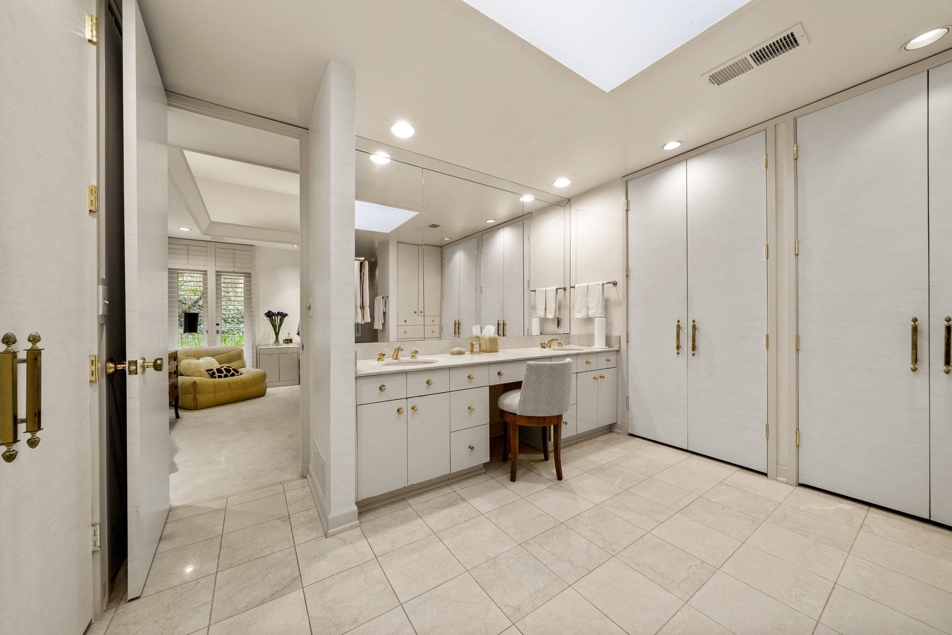 A bathroom with white cabinets , a sink , a chair and a skylight.