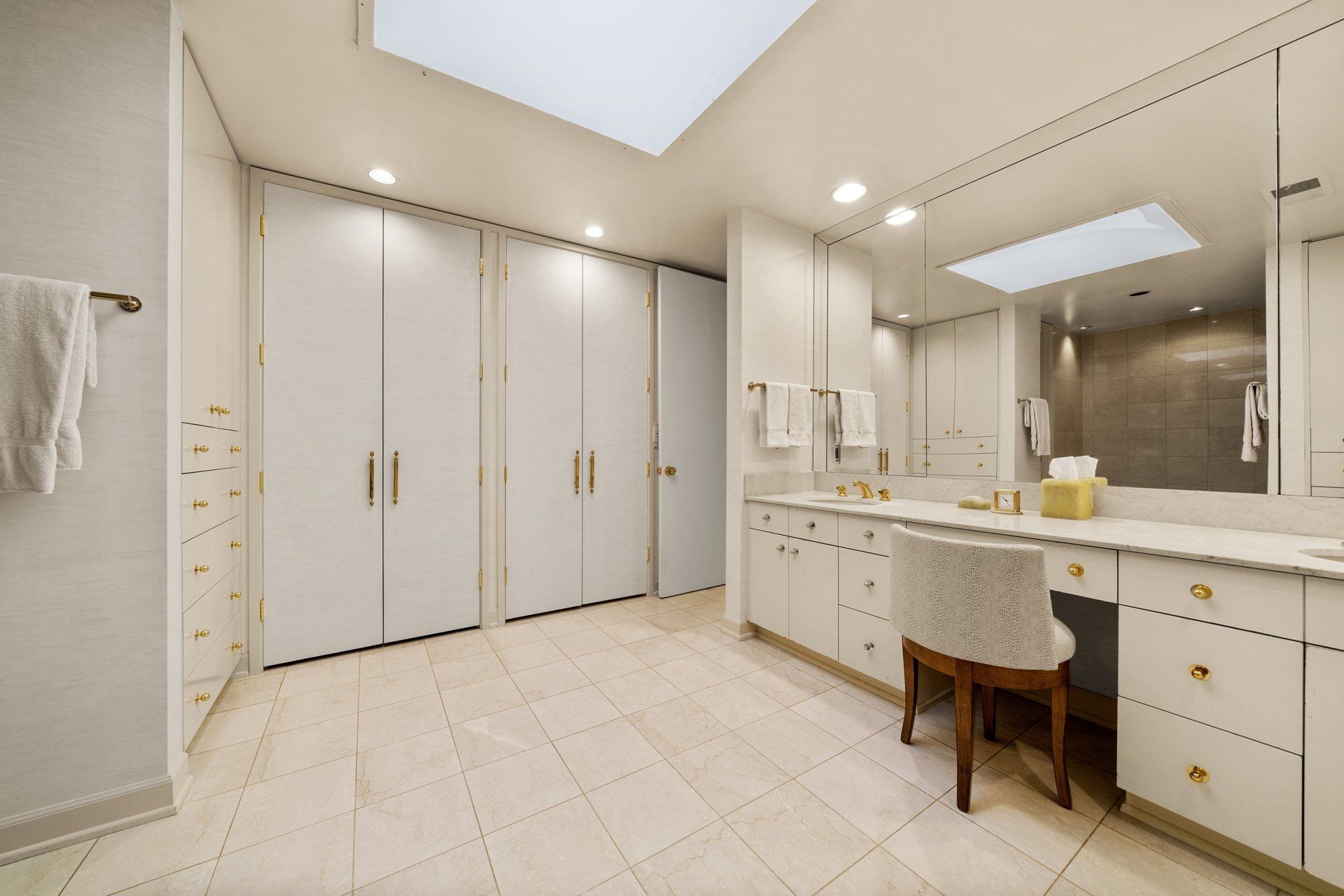 A bathroom with two sinks , a chair , a mirror and a skylight.
