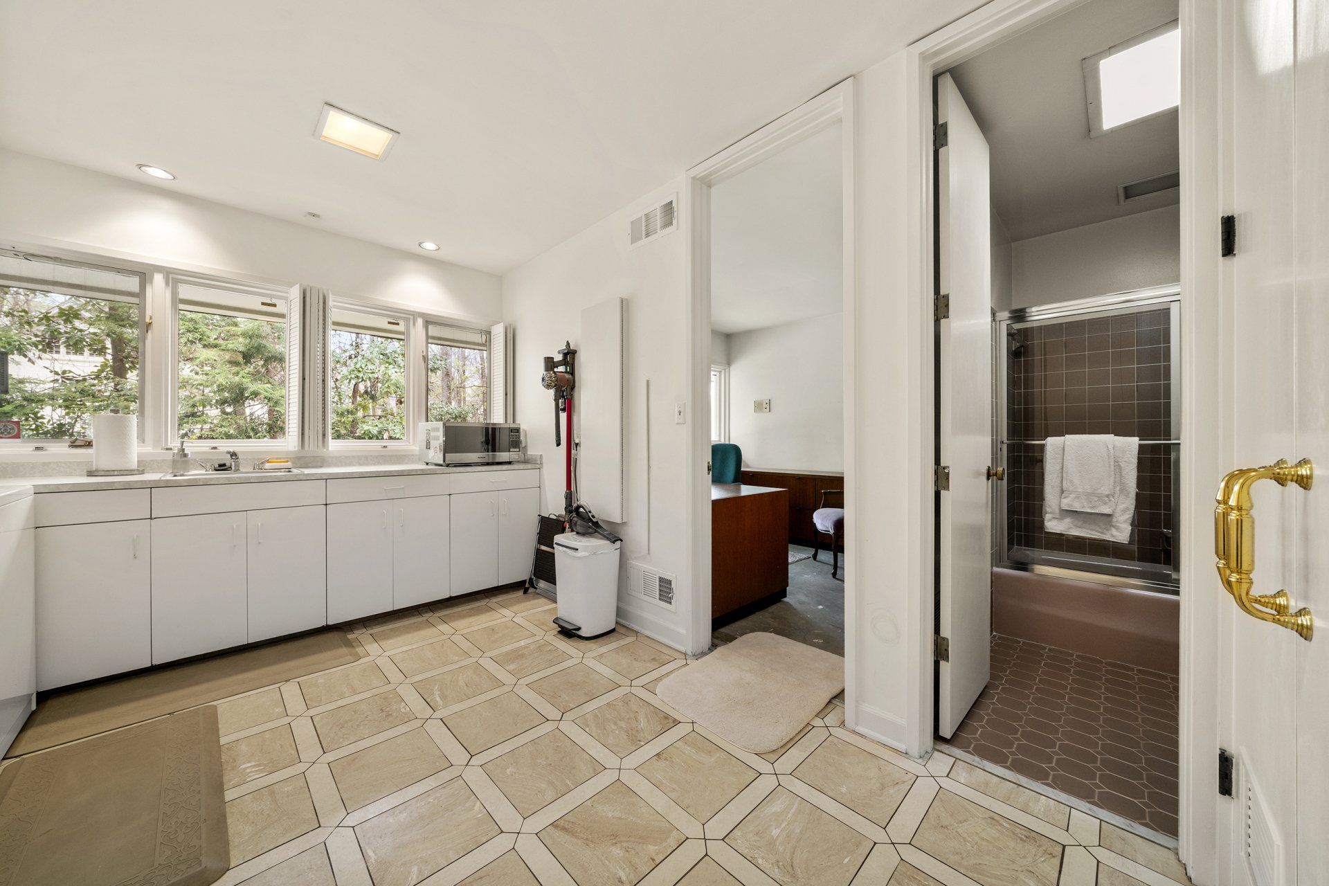 A laundry room with white cabinets and a tiled floor leading to a bathroom.